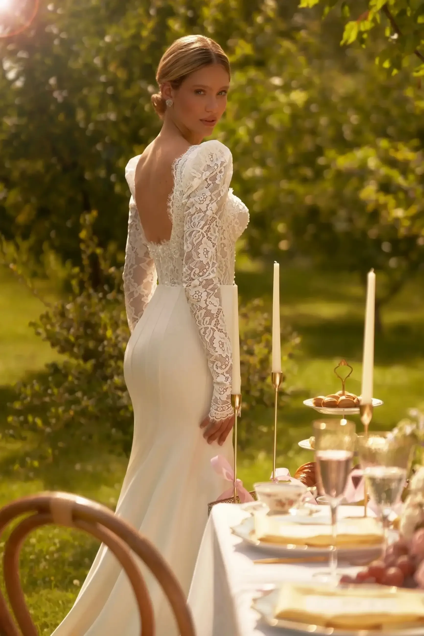 Model is wearing a fitted ivory mermaid wedding gown with a sweetheart neckline, embroidered corset, and long puffy sleeves attached to wide straps.