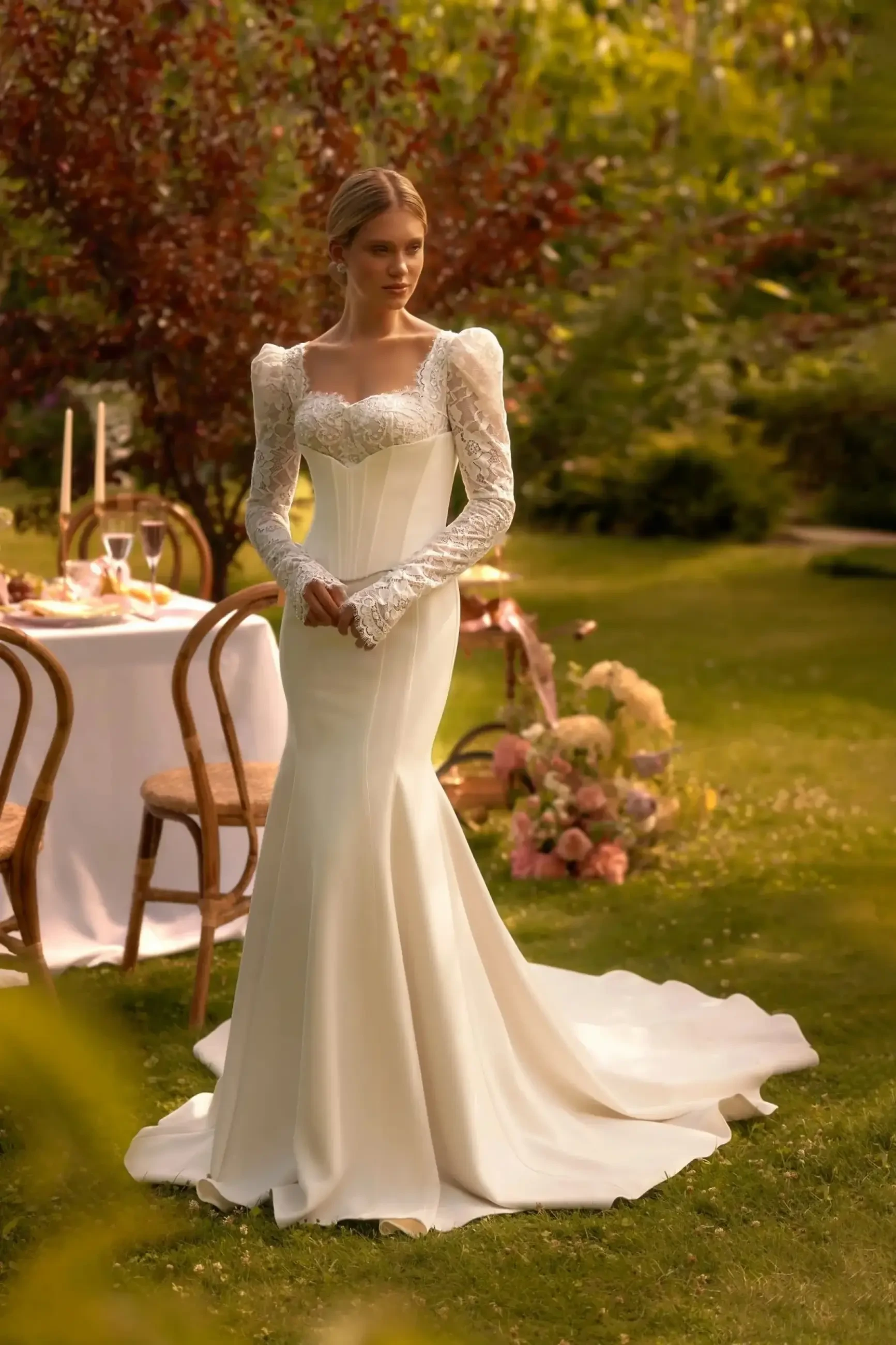Model is wearing a fitted ivory mermaid wedding gown with a sweetheart neckline, embroidered corset, and long puffy sleeves attached to wide straps.