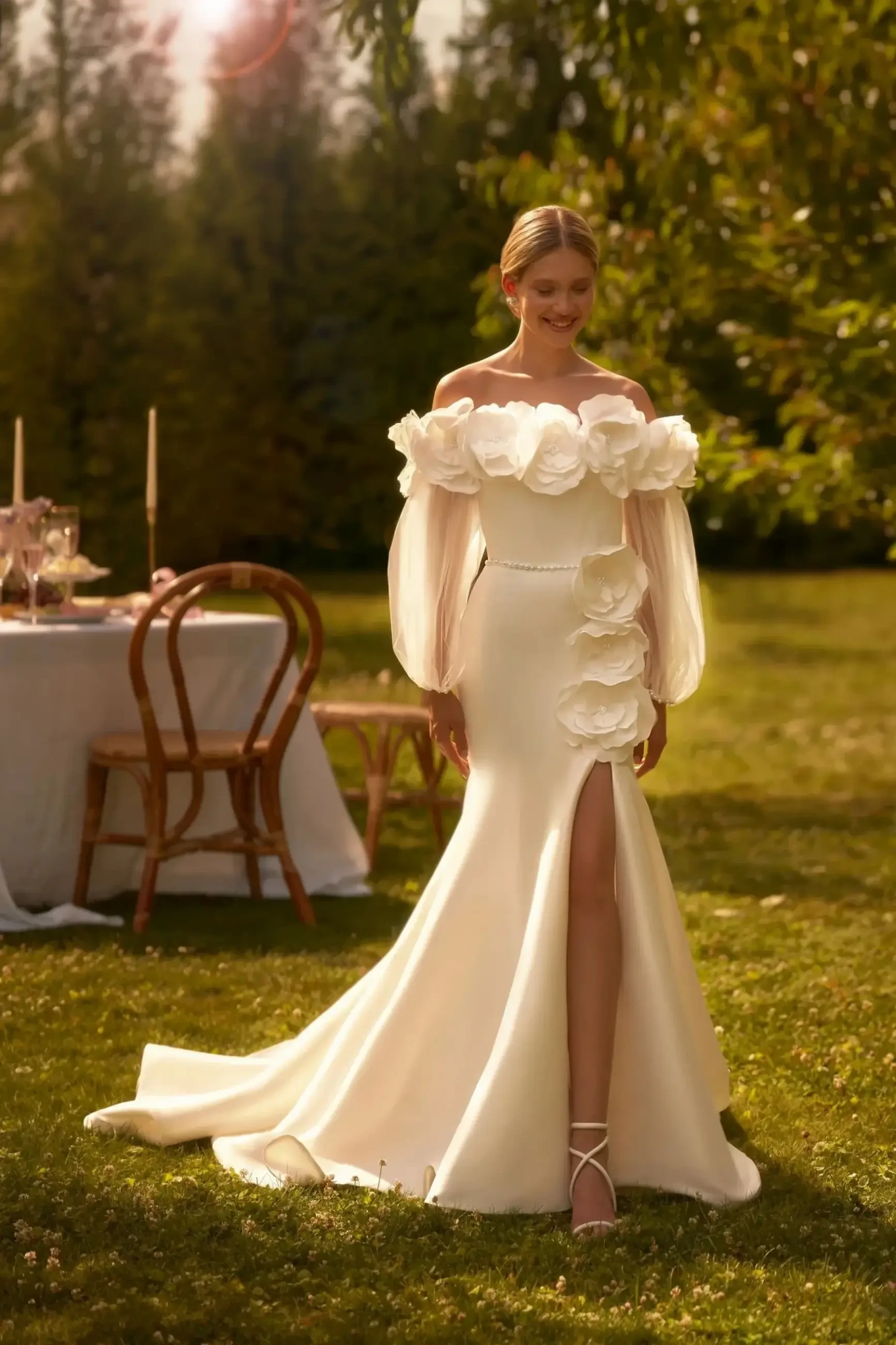 Model is wearing a sculpted mermaid wedding dress with 3D floral appliqués, a curly neckline, tulle puff sleeves, and a front slit.