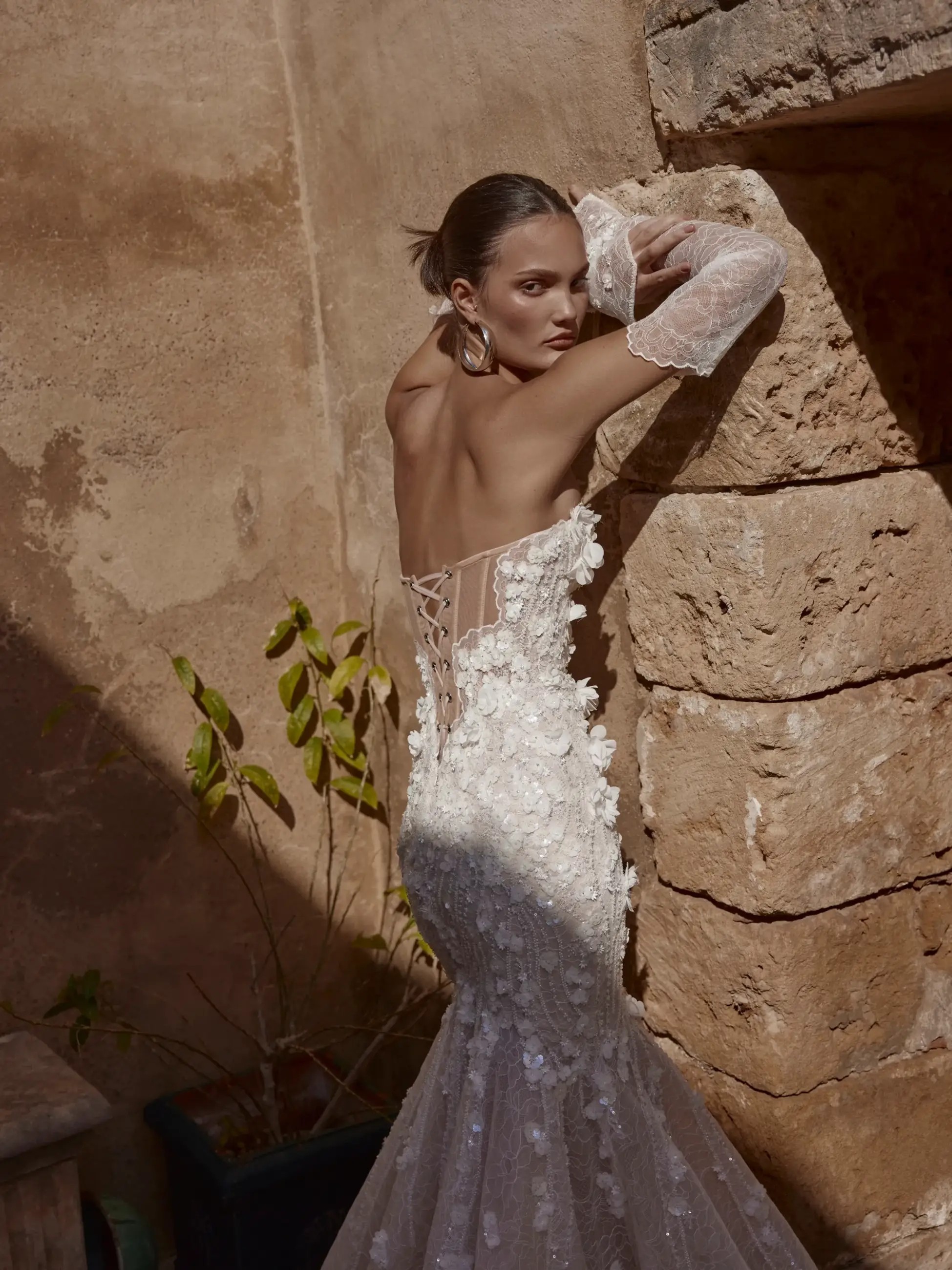 Model is wearing a wedding dress with a sweetheart neckline and intricate floral vines and lace
