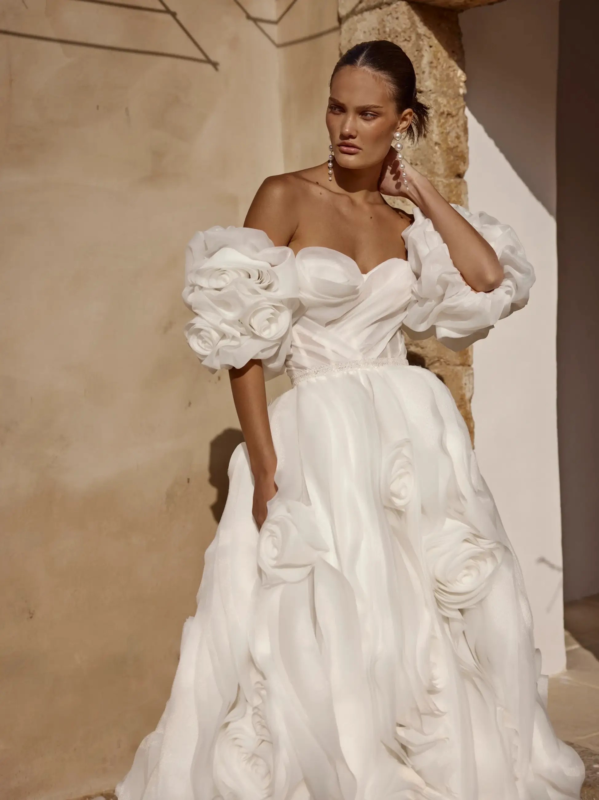 Model is wearing an off the shoulder organza wedding dress and a skirt with oversized roses