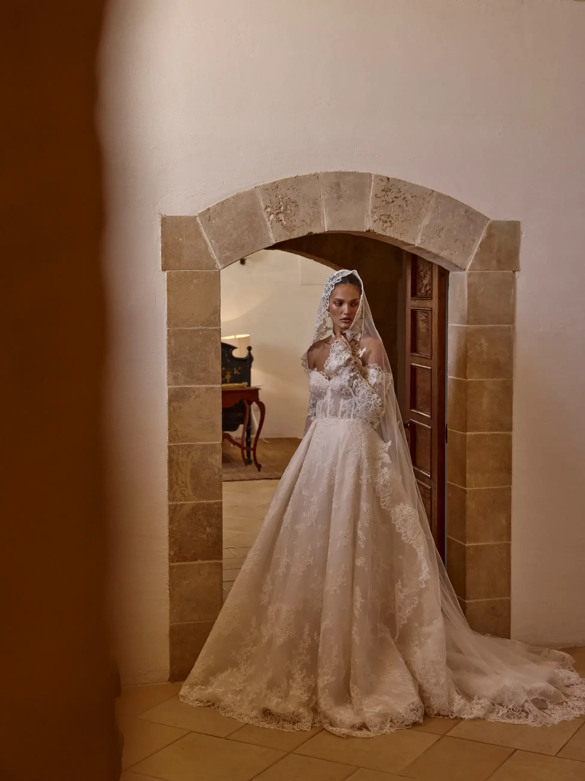 Model is wearing a corset princess dress crafted from intricate lace, featuring a fitted bodice, full skirt, and a matching veil.