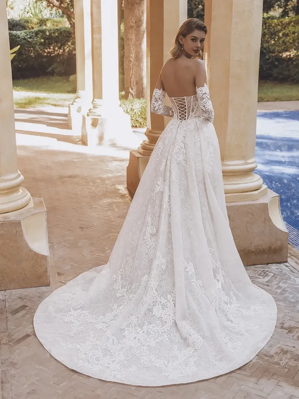Model is wearing a luxurious ball gown with sequin corded floral lace, off-the-shoulder long sleeves, and a pleated skirt slit.